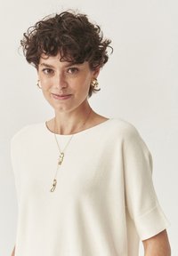 Top bianco a maniche corte realizzato in tessuto morbido, abbinato a orecchini a cerchio dorati e una collana con pendente dorato caratterizzata da un design testurizzato.