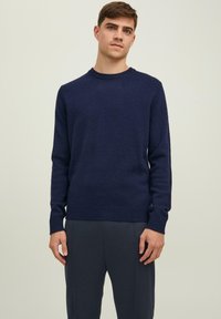 Granatowy sweter dzianinowy z okrągłym dekoltem oraz ściągaczami przy mankietach i u dołu. Gładka faktura; posiada długie rękawy i luźny krój.