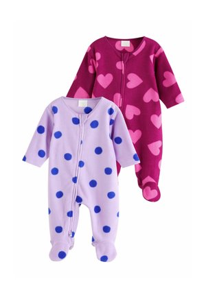 Baby wearing a purple polka dot onesie crawling on a quilted blanket with a small stuffed toy nearby in a living room setting.