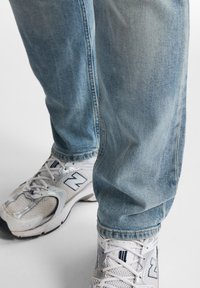 Jeans de mezclilla azul claro con un corte relajado y un ligero desvanecimiento, combinados con zapatillas deportivas blancas que cuentan con paneles de malla y acentos contrastantes.