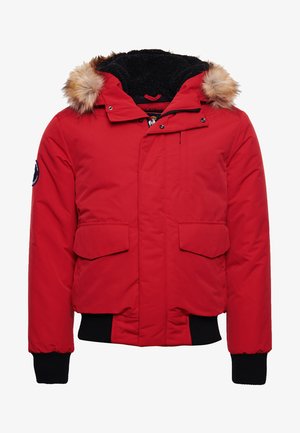 Red puffer jacket with a faux fur-lined hood, two front flap pockets, ribbed black cuffs, and a zippered closure. Soft, padded texture.