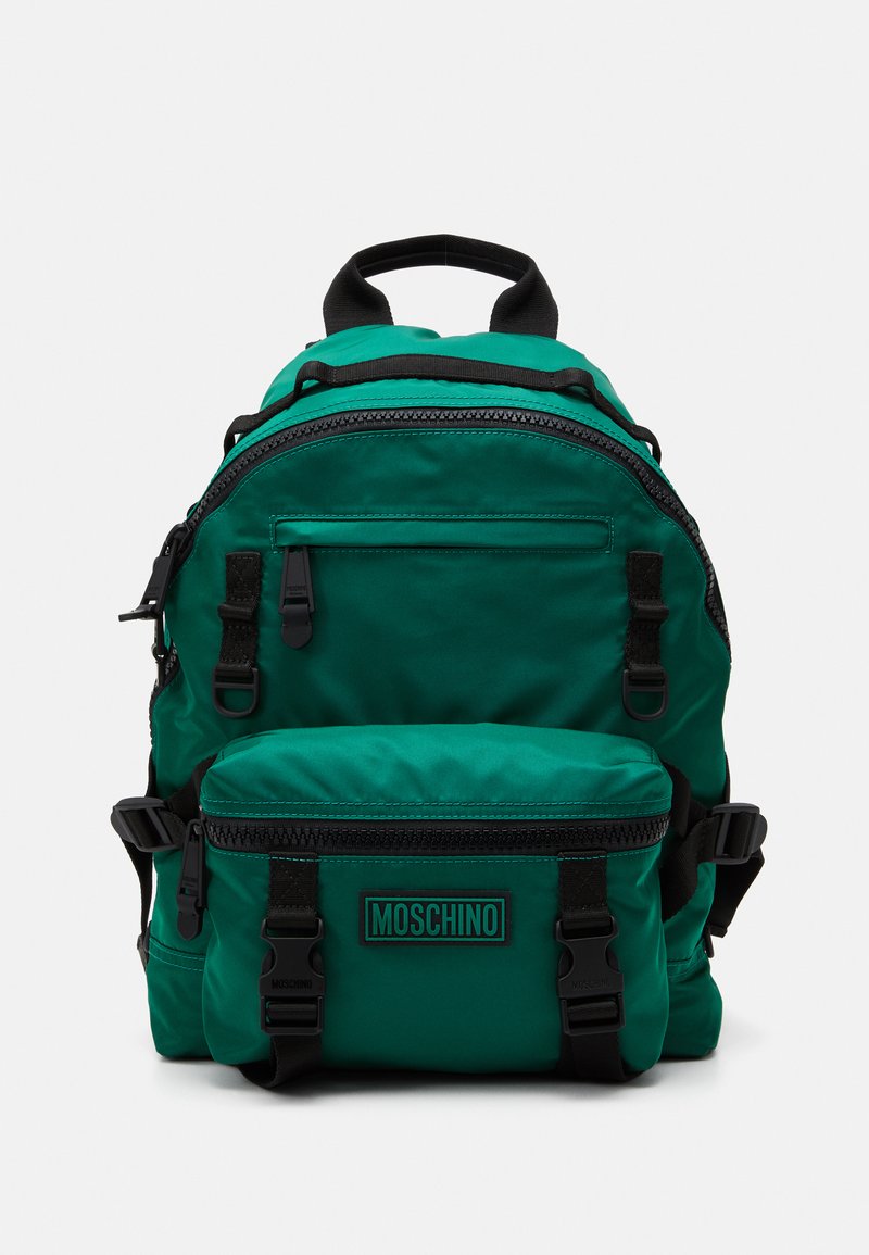 Grön nylonryggsäck med svarta detaljer, utrustad med flera dragkedjefack, justerbara remmar och ett framfack märkt "MOSCHINO."