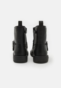 Botines negros de piel texturizada, con un tacón bajo, cremalleras en los laterales y un detalle de tira con una hebilla plateada.