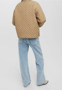 Chaqueta bomber beige acolchada con corte cuadrado, combinada con jeans de pierna ancha azul claro. La chaqueta presenta costuras en forma de diamante y bolsillos laterales.