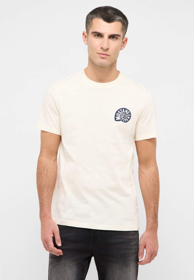 Cream-colored cotton t-shirt with a round neckline, short sleeves, and a navy blue graphic logo on the left chest area.