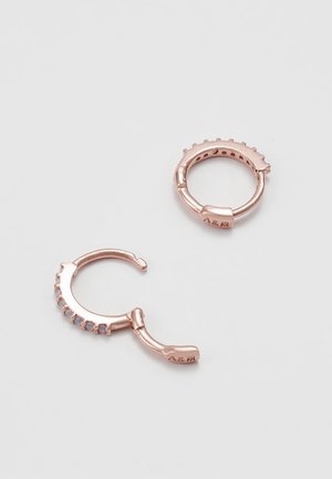 Deux petites créoles en or rose avec une fermeture à charnière, dont une ornée de petites pierres claires sur le bord extérieur.