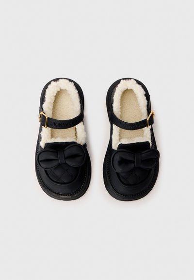 Sorte slip-ons med quiltet design, en myk hvit foring, en sløyfeaccent og en stropp med gullfarget spenne for sikker passform.