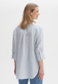 Light blue striped shirt with a relaxed fit, buttoned cuffs, and a rounded hem. Made of soft fabric with a lightweight texture.