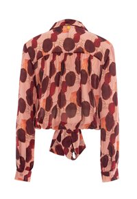 Blouse courte en tissu rose clair avec des motifs floraux rouge foncé, manches longues, poignets à boutons et ourlet avant noué.