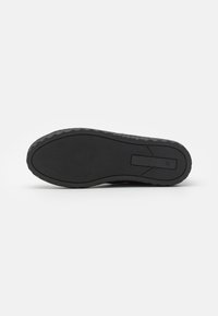 Black rubber shoe sole featuring textured grip pattern and a smooth border. Includes a rectangular logo detail embedded on the side.