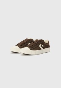 Sneakers in camoscio marrone con punta e suola in gomma beige. Presentano un design con lacci e un logo a stella bianca sul lato esterno.
