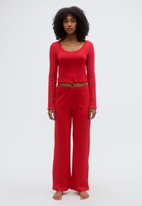 Ensemble deux pièces côtelé rouge composé d'un haut à manches longues avec encolure dégagée et d'un pantalon à jambes larges avec taille à cordon. Texture douce et coupe décontractée.