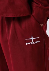 Pantaloni in tessuto bordeaux con logo "PXP" bianco ricamato, texture liscia e design a gamba dritta con tasche laterali.