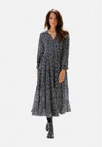 Langes, schwarzes Blumenkleid mit langen Ärmeln, V-Ausschnitt, gerafftem Bund, fließendem Rock und weichem, leichtem Material. Kombiniert mit schwarzen Stiefeln.