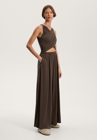 Braunes Zweiteiliges Outfit mit einem ärmellosen Oberteil mit Raffung und einer hoch taillierten, weit geschnittenen Hose. Weicher Stoff mit glatter Textur.