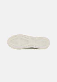 White sneaker sole with textured rubber, featuring a patterned tread for grip and a subtle brand logo near the heel.