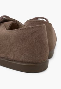 Scarpe slip-on in suede marrone con una suola in gomma scura bassa e dettagli cuciti; presentano un retro aperto e un tacco arrotondato.