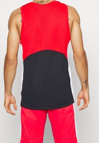 Débardeur de sport rouge et noir avec une texture en maille, doté d'accents latéraux blancs et d'un ourlet arrondi. Vue arrière montrant les détails des épaules et des bras.