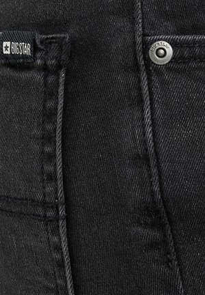 Mustast denimist kangas, kus on nähtavad taskusaumad, metallnõel „BIG STAR“ templiga ning must kangasilt, millelt loeb „BIG STAR“ ja mis kannab tähelogot.