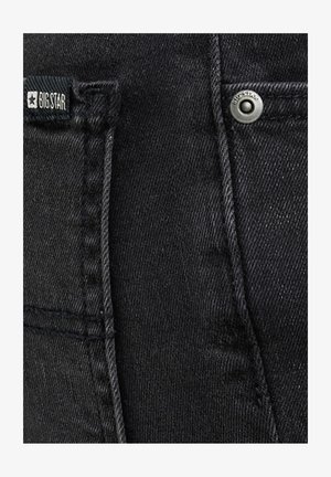 Mustast denimist kangas, kus on nähtavad taskusaumad, metallnõel „BIG STAR“ templiga ning must kangasilt, millelt loeb „BIG STAR“ ja mis kannab tähelogot.