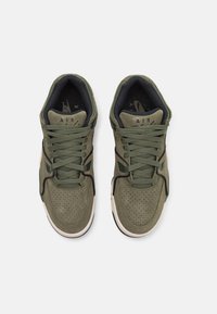 Vihreät mokkakenkä, joissa on reikäkuvioitu kärki, pehmustettu nilkkapanta ja mustat yksityiskohdat. Sisältää litteät nauhat ja valkoisen kumipohjan.