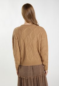 Sweter dziany w kolorze camel z teksturowanym wzorem w diamenty, z prążkowanymi mankietami i dolnym wykończeniem. Stylizowany na brązowej spódnicy z wzorem w warstwy.