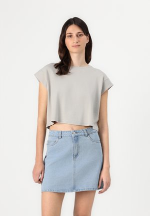 T-shirt cropped grigio chiaro con maniche corte abbinato a una mini gonna in denim blu chiaro con chiusura a bottoni e tasche frontali.