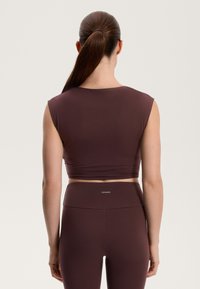 Burgundski crop top s kratkim rukavima, izrađen od glatkog materijala. Uparen s tajicama visokog struka koje prikazuju mali logo na pojasu.