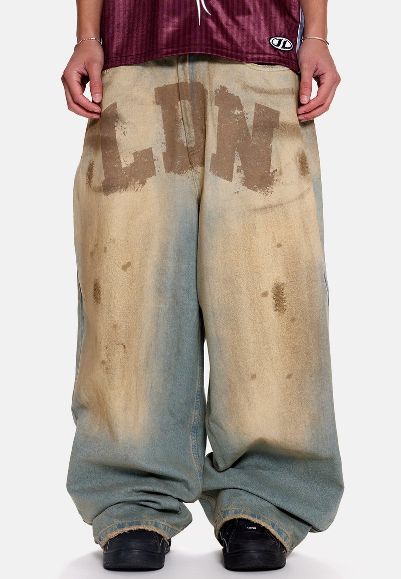 Φαρδιά τζιν παντελόνια σε ανοιχτό μπλε και μπεζ με εφέ πλυσίματος οξέος. Διαθέτουν μεγάλο, ξεθωριασμένο κείμενο "LDN" σε καφέ χρώμα στο εμπρός μέρος.