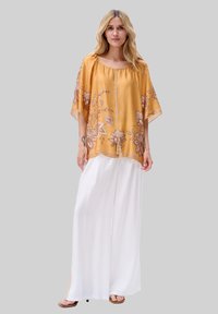 Żółta bluzka z haftem kwiatowym z szerokimi rękawami, zestawiona z białymi, zwiewnymi spodniami palazzo. Lekki materiał o luźnym kroju i casualowym designie.