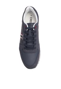 Zapatilla deportiva azul marino con parte superior de cuero texturizado, que presenta franjas blancas y rojas, un cuello acolchado y una suela de goma. Los cordones son de color azul oscuro.