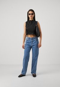 Top corto negro con detalles fruncidos, cierre de cremallera, combinado con jeans de talle alto azul claro y zapatos planos negros. Los accesorios incluyen gafas de sol negras.