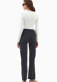 Vaqueros negros de talle alto con pierna recta, cinco bolsillos y cierre de botón. Combinados con una blusa ajustada de manga larga blanca.