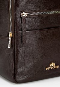 Sac en cuir marron avec une finition texturée, doté d'une fermeture éclair dorée et d'un accent de logo. Comprend une poche latérale fermée par une fermeture éclair.