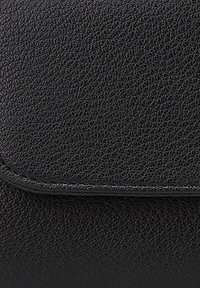 Sac en cuir noir texturé avec une fermeture à rabat magnétique et des bords lisses, mettant en avant son design minimaliste et son matériau durable.