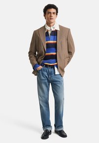 Brun houndstooth-blazer, blåstripet genser, hvit skjorte med krage, lyseblå jeans, svarte sko. Uformell lagdelt antrekk med varierte teksturer.