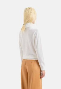 Maglione bianco a collo alto con maniche lunghe, design aderente, orlo a costine. Abbinato a pantaloni beige a vita alta e gamba larga.