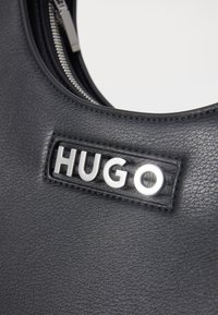 Black leather handbag with a smooth texture, featuring a silver "HUGO" logo and zipper detail. Simple, rounded design.