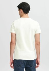 Tricou alb cu guler rotund, mâneci scurte, design simplu, textură moale, purtat împreună cu blugi albastru închis, perspectiva arată partea din spate fără logo-uri sau modele.