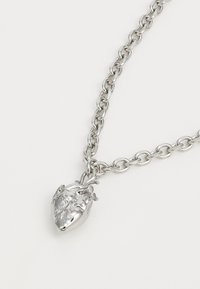 Silver necklace featuring a detailed heart pendant. The chain is composed of linked oval shapes, providing a textured appearance.