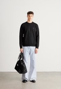 Čierna mikina s okrúhlym výstrihom, voľné svetlomodré rifle a čierna taška tote. Hladká textúra, minimalistický dizajn s malým logom.