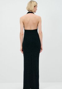 Schwarzes Halsband-Maxikleid mit offenem Rücken, das eine figurbetonte Silhouette hat und kleine weiße Punkte im gesamten Stoff aufweist.
