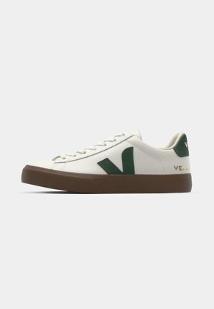 White sneaker with green V logo, stitched details, and brown rubber sole. Features laces and a textured fabric finish.