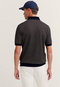 Dunkelblaues Poloshirt mit strukturiertem Muster, ausgestattet mit einem gerippten Kragen und Ärmeln. Kombiniert mit weißen Hosen und einer blauen Mütze.