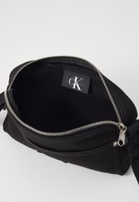 Borsa in tela nera con chiusura a zip, dotata di un'etichetta interna. Il design presenta linee semplici e una texture morbida.