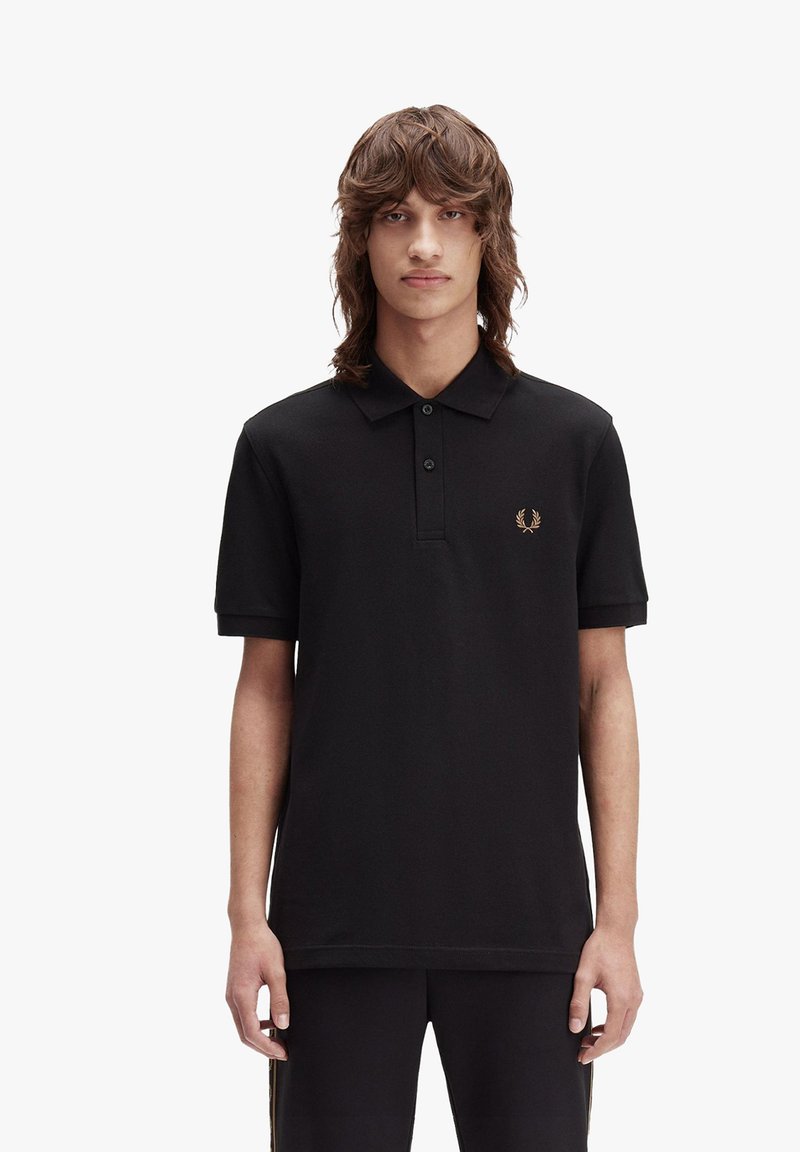 Svart bomullspolo med krage, tre knappslå, och en guld broderad logotyp på bröstet. Korta ärmar med uppvikta avslut.