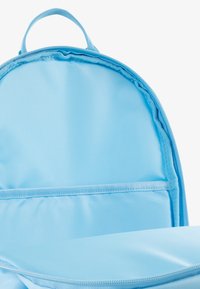 Light blue backpack interior with smooth nylon fabric. Features a zippered main compartment and a flat pocket against the back panel.
