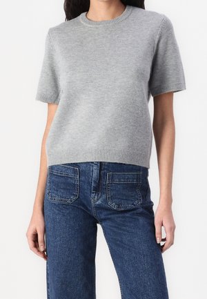 Kvinde iført en lysegrå kortærmet striktrøje kombineret med højtaljede blå denimjeans med forlommer.