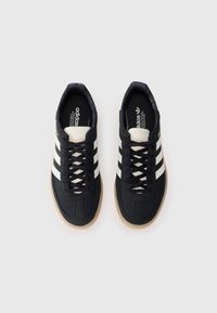 Black athletic sneakers with three white stripes, textured fabric, and a brown rubber sole. Logo printed on the tongue and side.