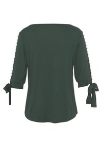 Dunkelgrünes Oberteil mit Dreiviertelärmeln, Bindebändern an den Manschetten und dekorativen Knöpfen entlang der Seitennaht. Glatte Stoffoberfläche.